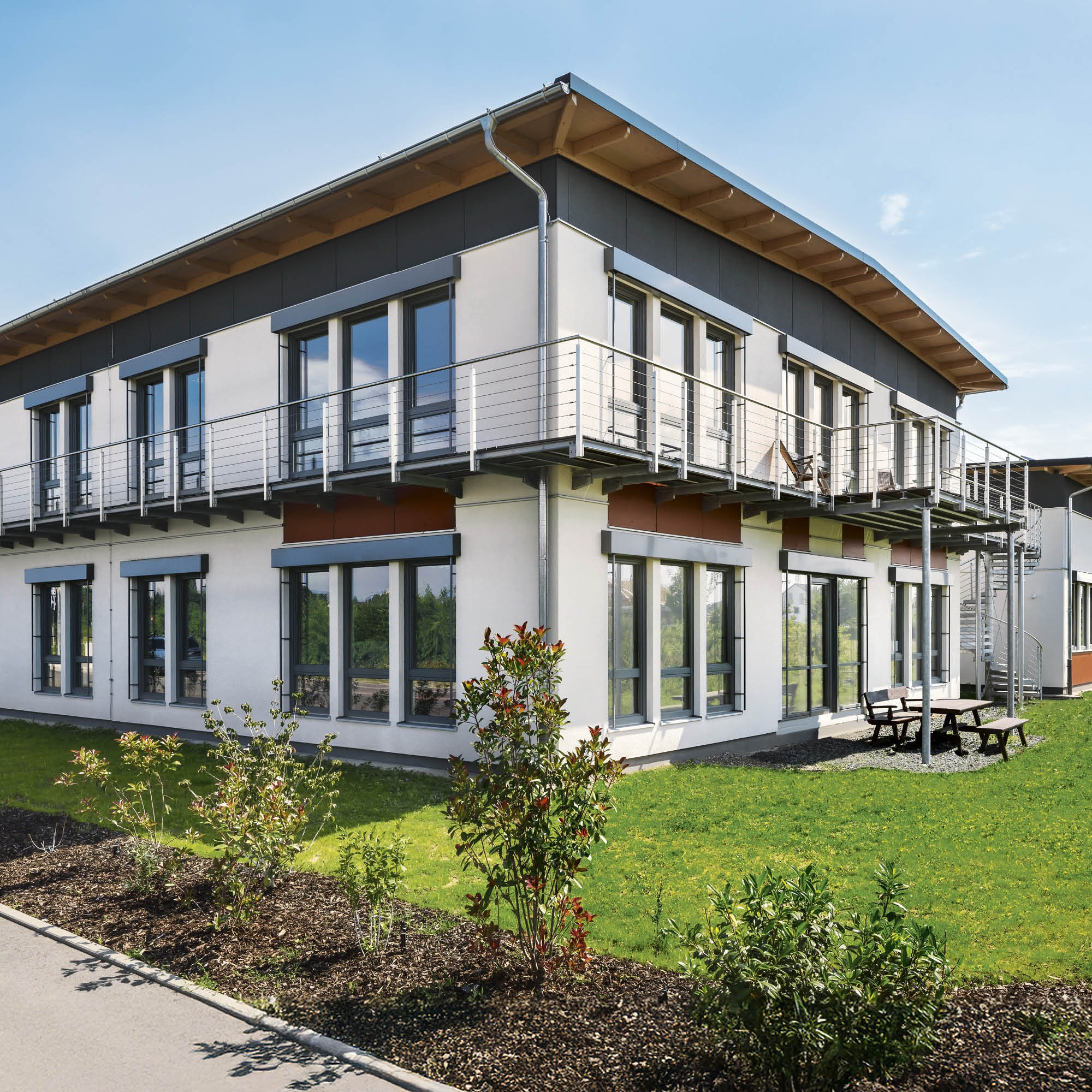 Modernes Bürogebäude mit weißen Fassaden, umlaufenden Balkonen, großen Fenstern und einer Außentreppe.