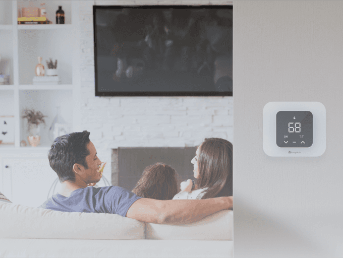 A family in the living room with a thermostat installed on the wall