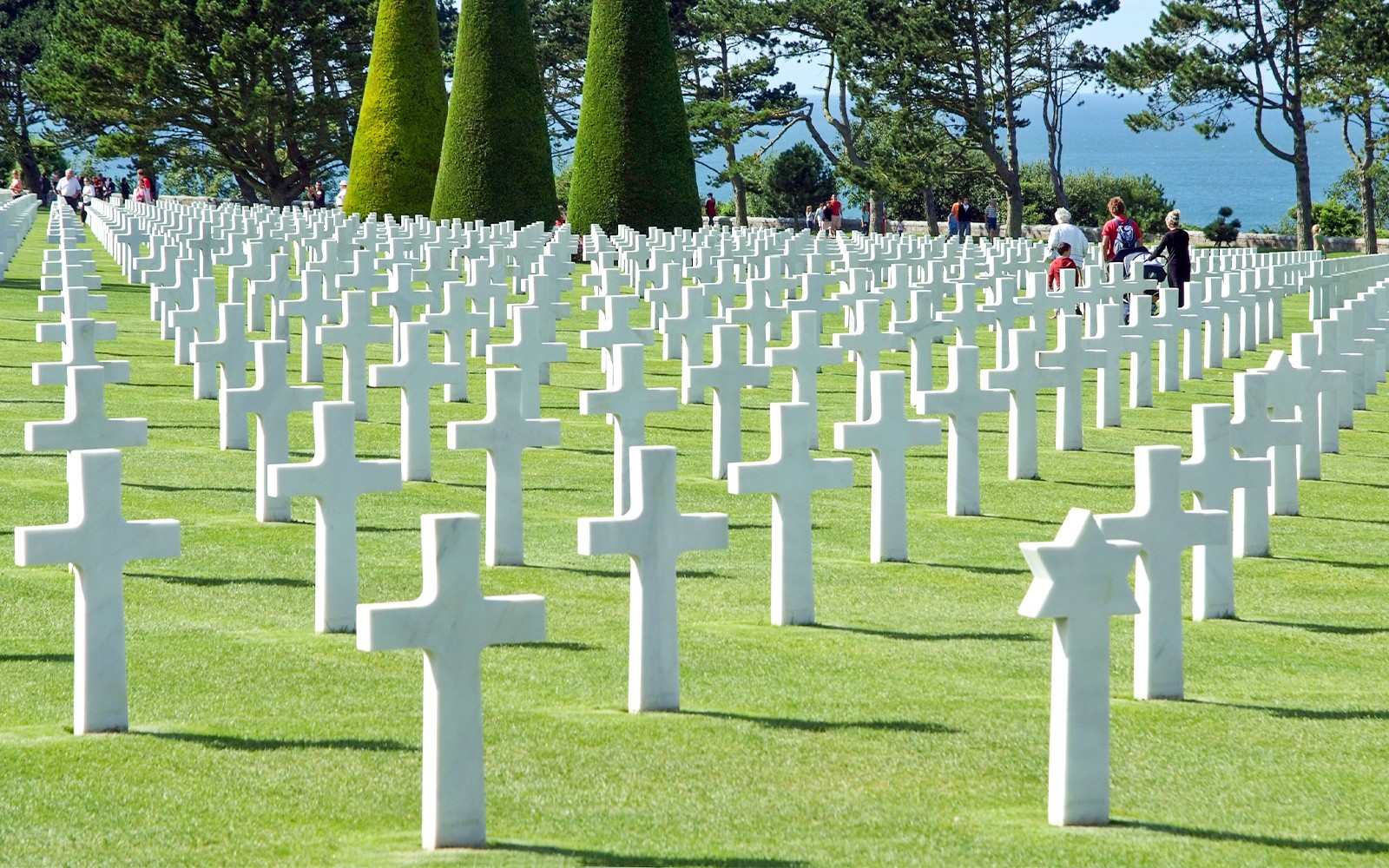 Rows of white crosses at Normandy American Cemetery, France, with visitors walking among them.