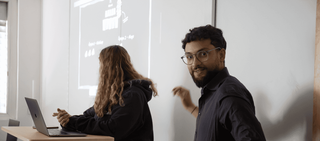 Deux personnes dans une salle de réunion faisant une présentation, l’une avec un ordinateur portable, et l’autre souriant face à l’appareil photo.