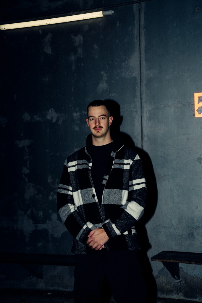 Portrait with direct flash of a young man standing against a wall