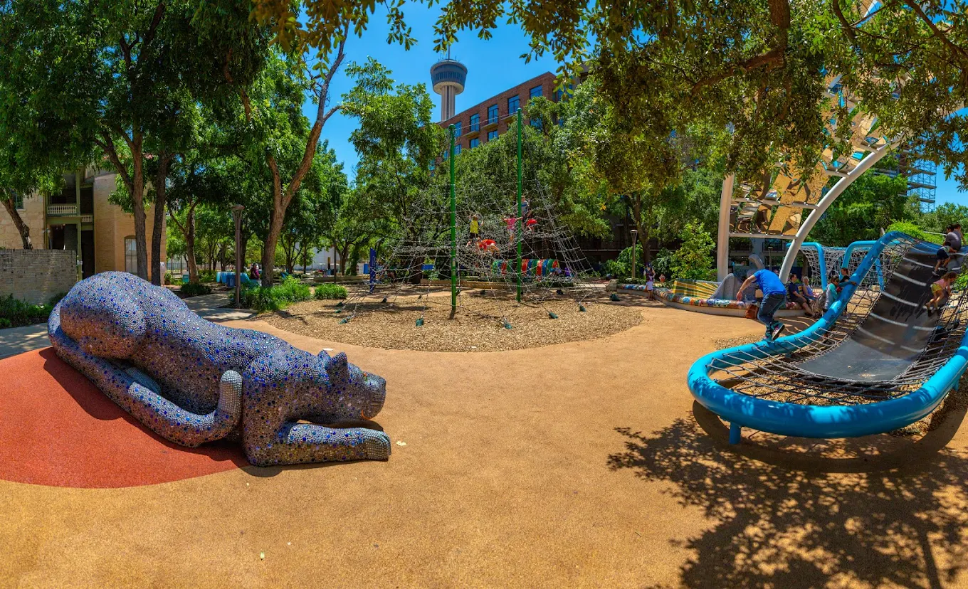 Children's playground with a mosaic panther sculpture and climbing net structures, Tower of the Americas visible in the background
