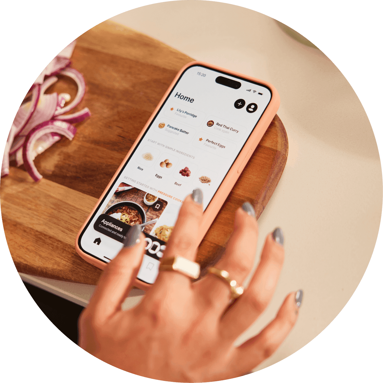 Hand taps a smartphone showing a cooking app home screen on a wooden cutting board beside sliced red onions