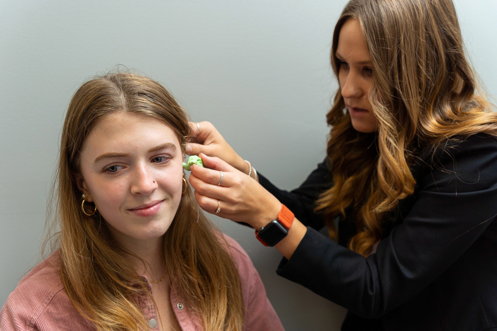 A stylist is applying hair extensions to a young woman's hair in a salon setting.