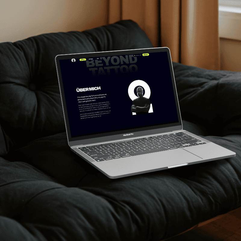 Silberndes Macbook mit nachtblauer über mich sektion eines Webdesigns im Display, stehend auf einer schwarzem Couch