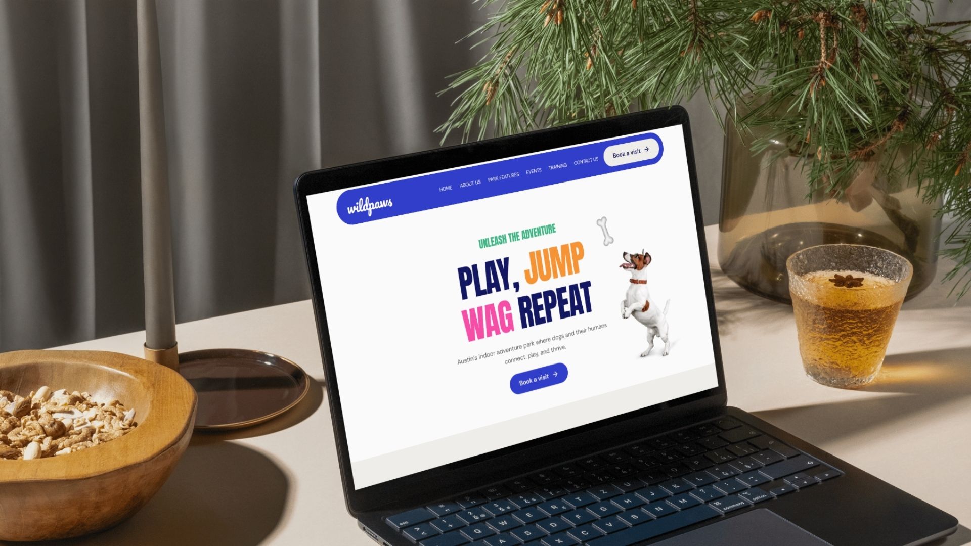 Hero section with the words play, jump, wag, repeat in bold colors and a dog jumping to get a bone, displayed in a laptop mockup set on a table