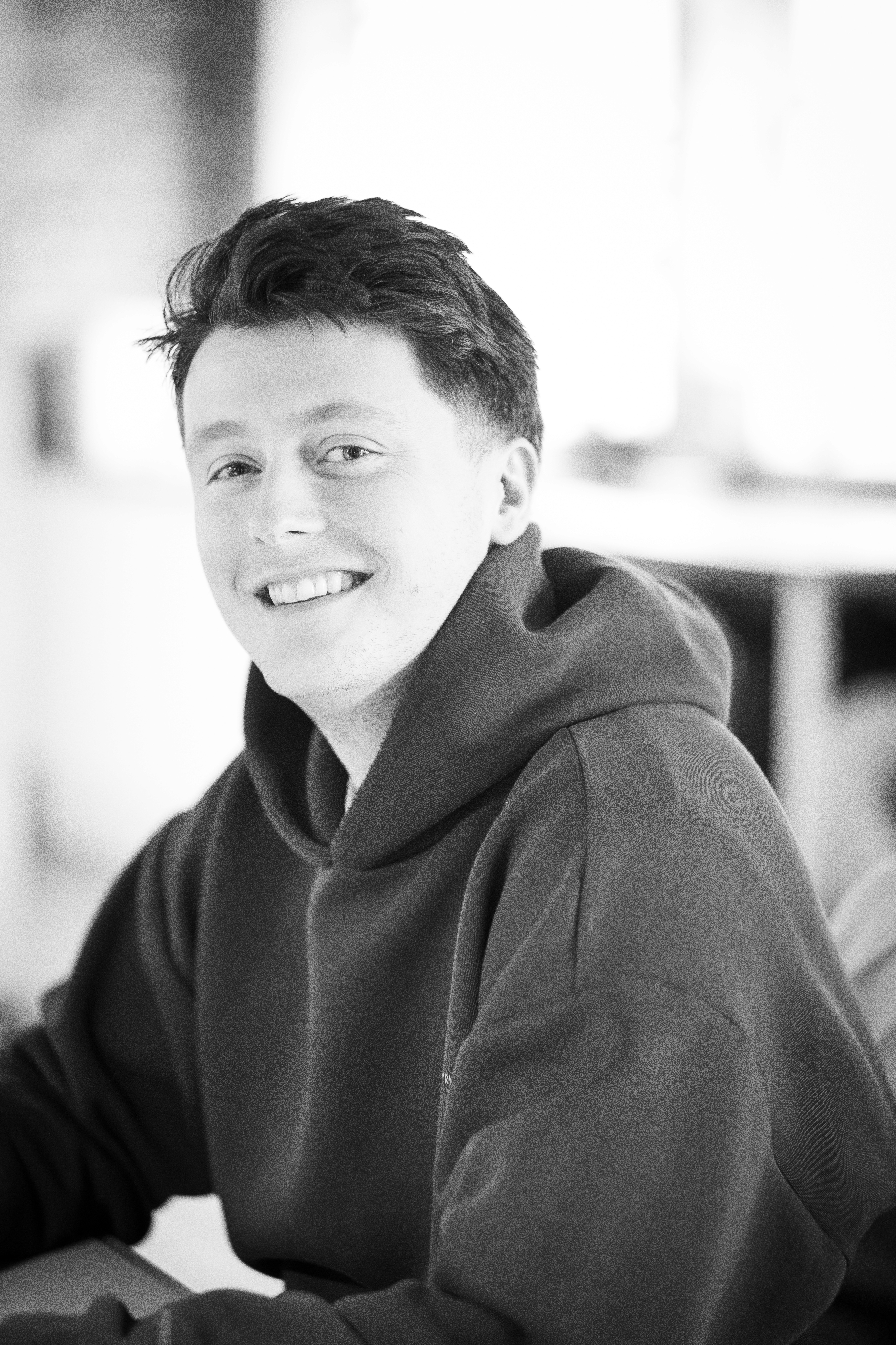 A thoughtful young person with dark hair gazes to the side, captured in soft black and white lighting.