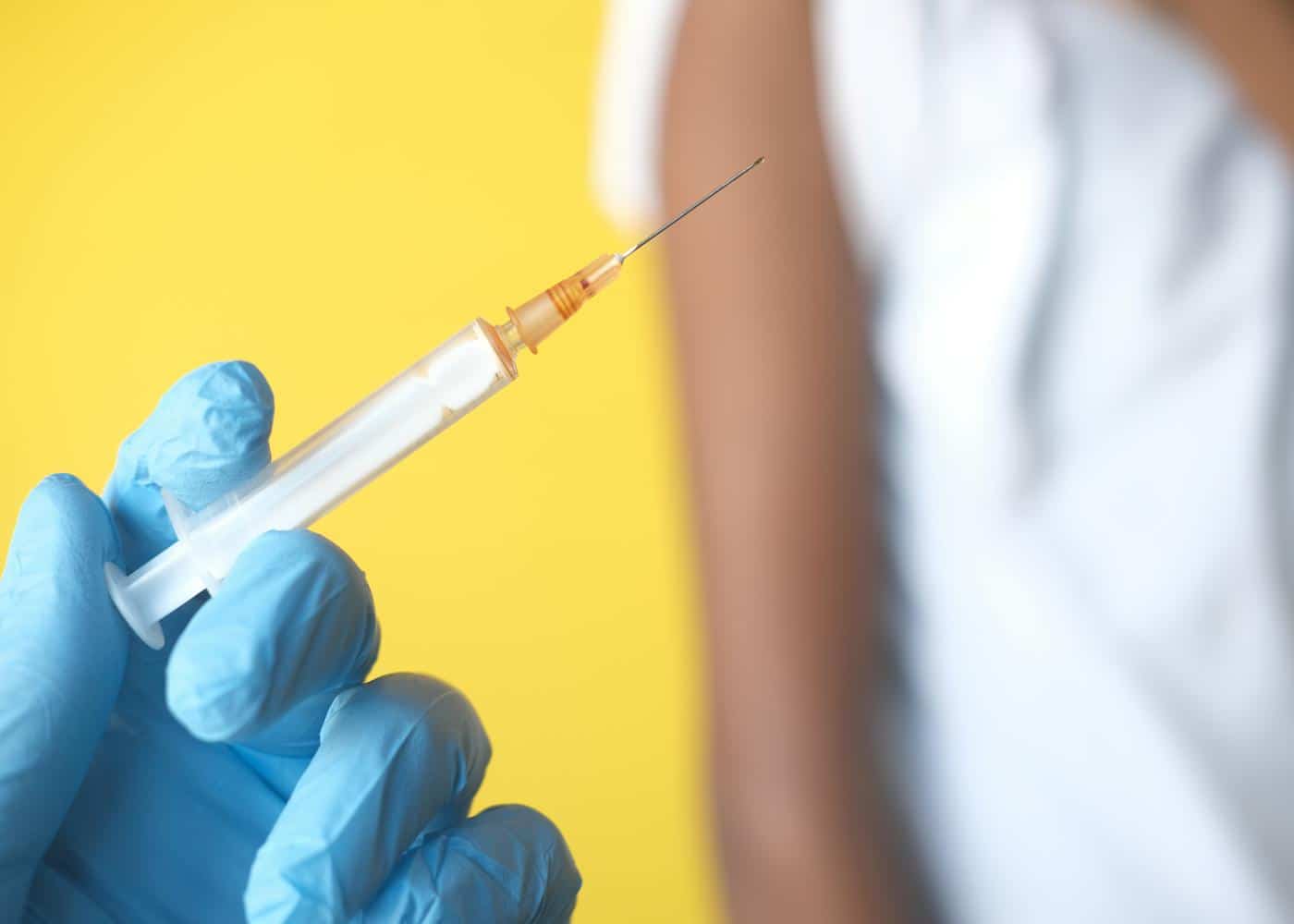 Gloved hand holding a syringe against a yellow background