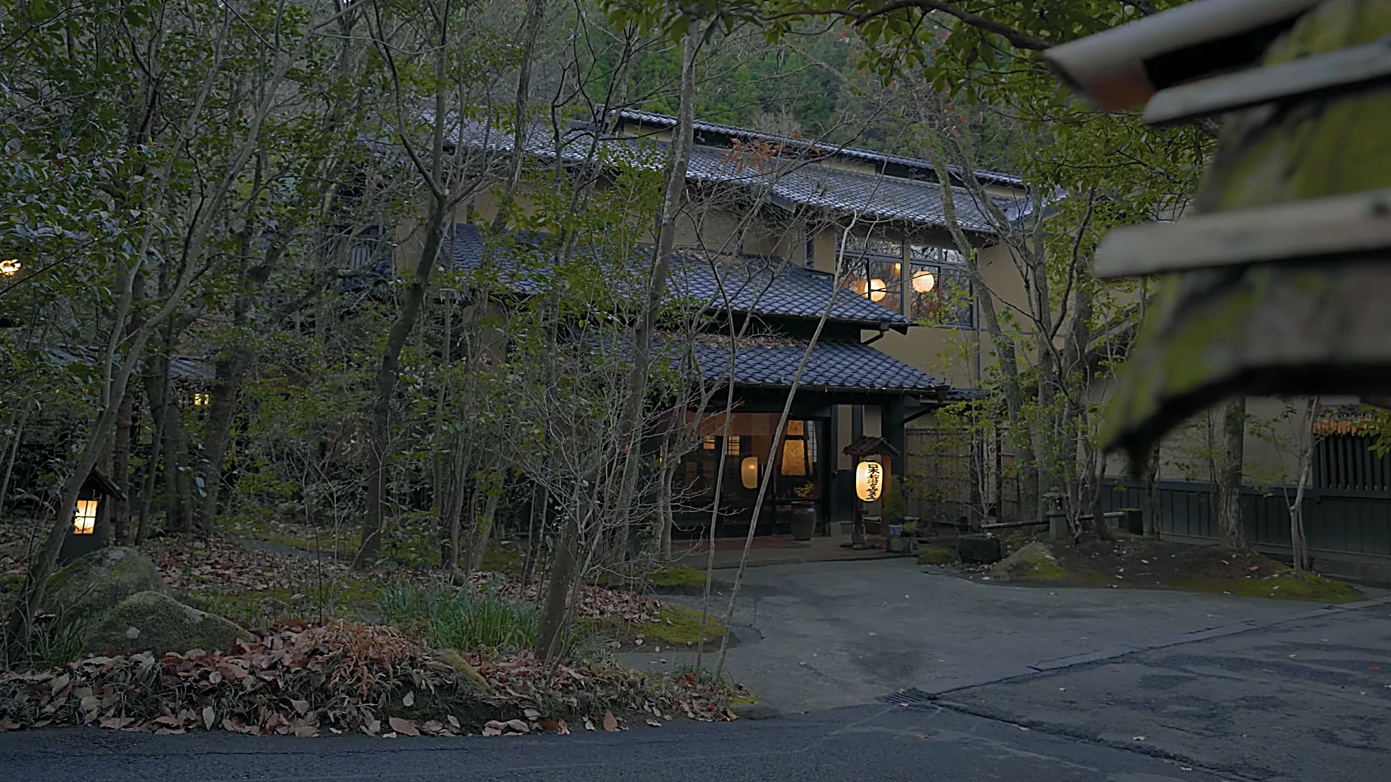 An inn exterior at Kurokawa Onsen at dusk, entrance lit, gravel forecourt in front