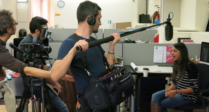 A photo of a group of people filming a scene in an office.