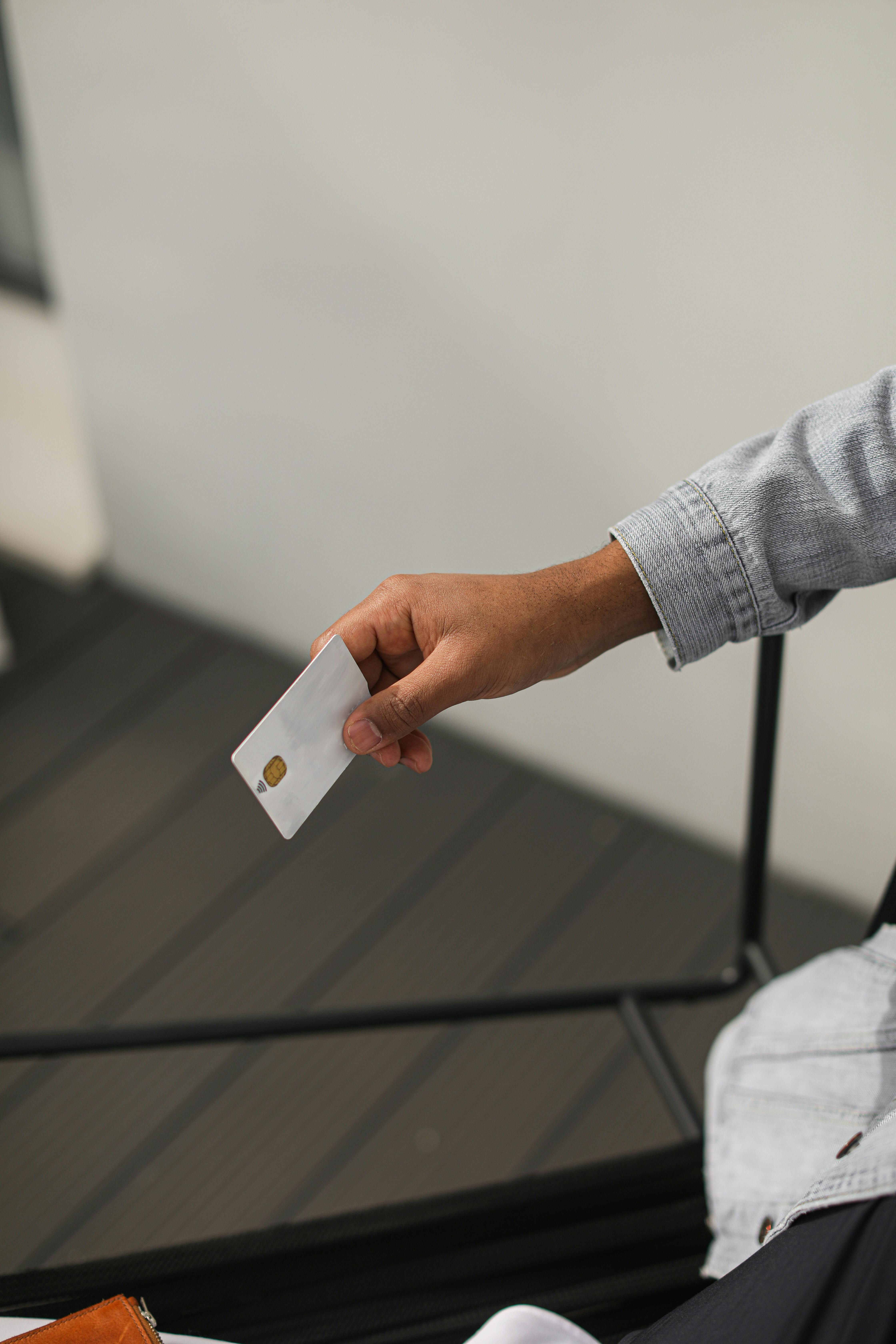 A person in a denim jacket holds out a small, white chip card against a neutral background.