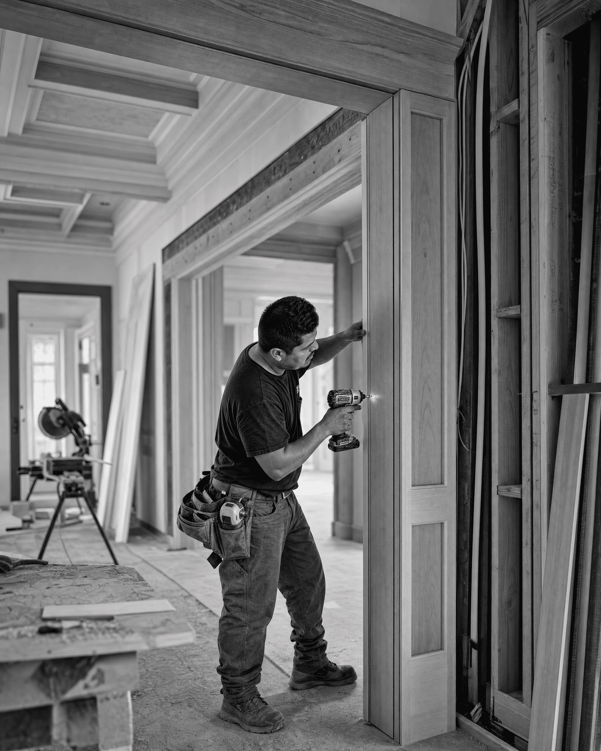 Construction professional fastening wood doorway trim with a cordless drill during an active interior renovation.