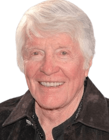 A warm, close-up portrait of an elderly man with white hair, smiling brightly. He is dressed in a casual dark jacket, exuding a friendly and lively demeanor. The outdoor setting with soft, blurred greenery in the background adds a relaxed and approachable atmosphere to the image.