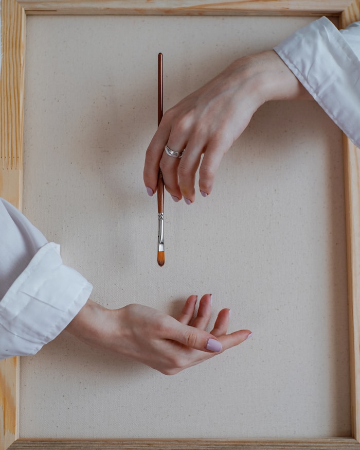 Hands holding a paintbrush over a blank canvas.