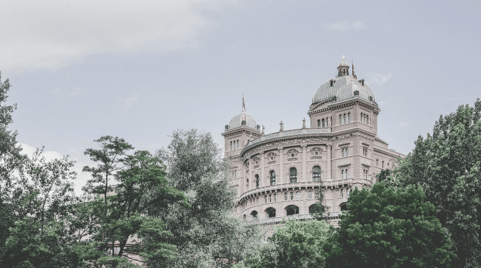 View of the Swiss Federal Palace surrounded by trees, symbolizing the role of the government in shaping policies and regulations for sustainable mobility and electromobility initiatives in Switzerland