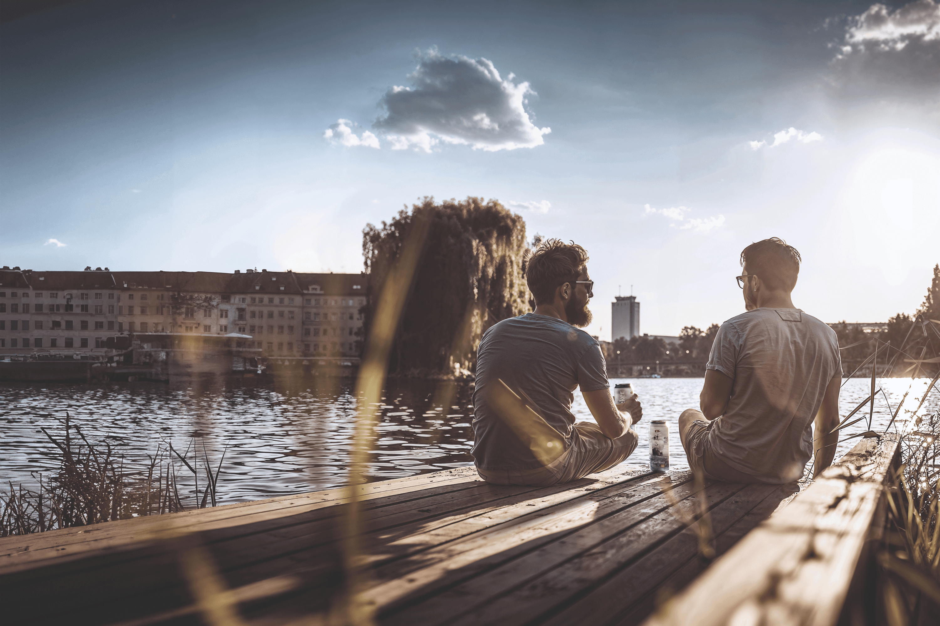 Two men sit on a dock, drinking beer