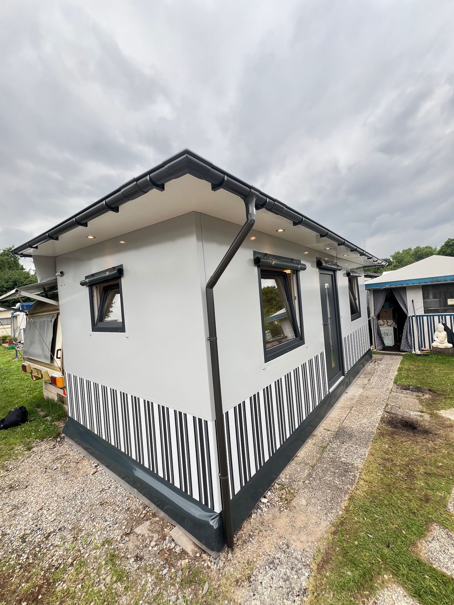 Dauerstandvorzelt-Camper mit schwarz-weißer Außenseite, gestreiftem Vorzelt, Sitzecke unter bewölktem Himmel, mit vielseitigem Zeltdesign.