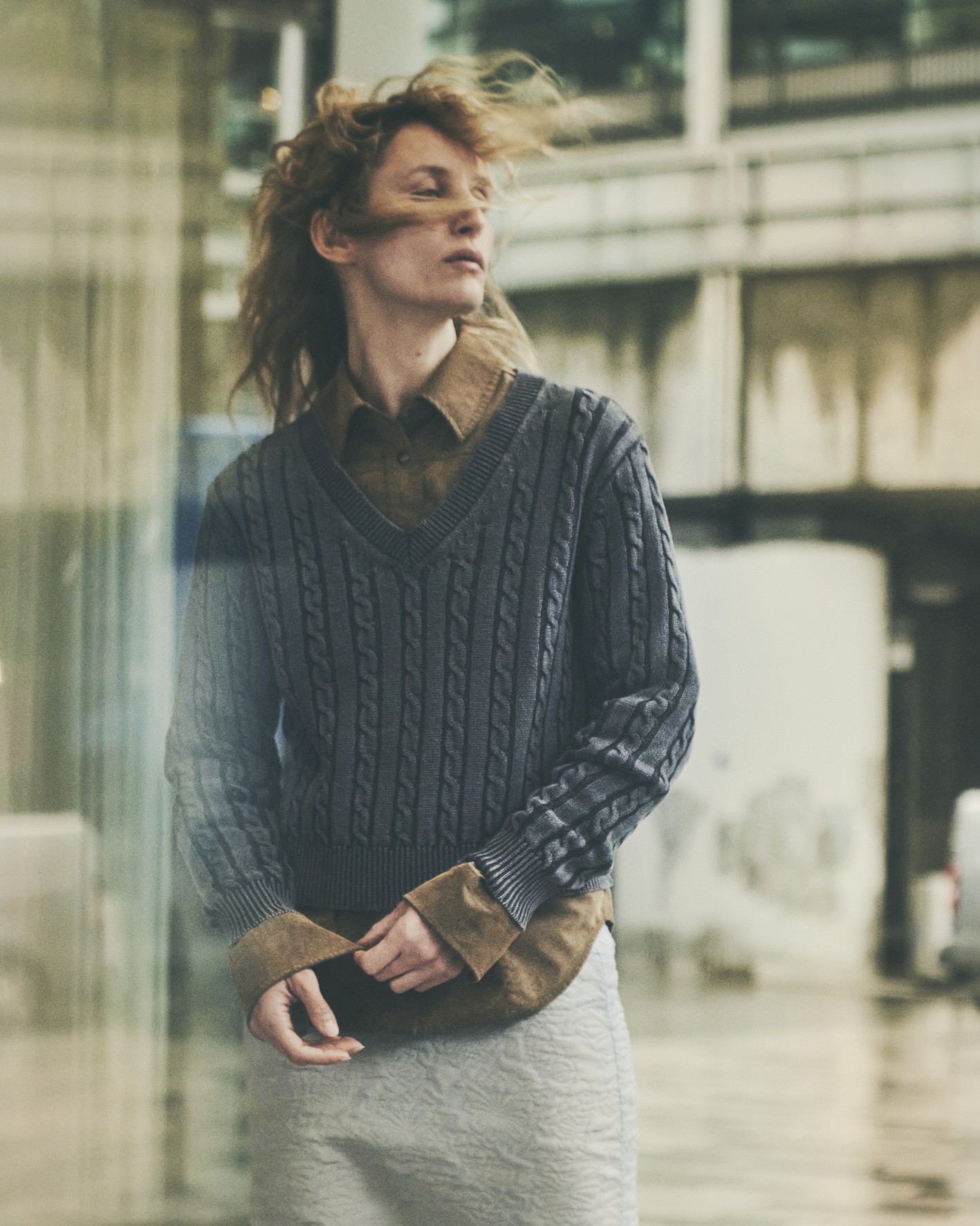 Une femme porte un pull à torsade et une chemise beige dans une photo façon mode 