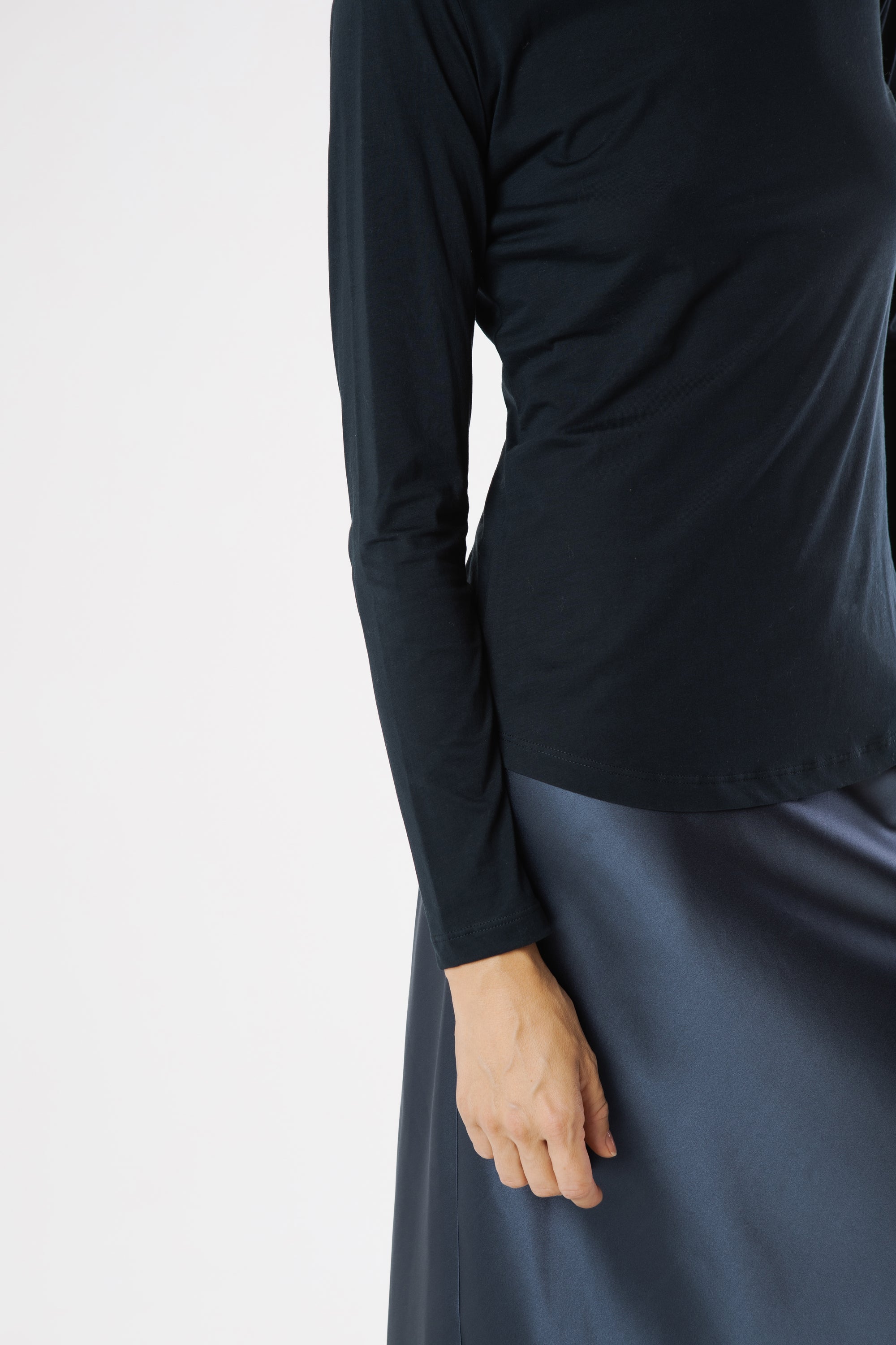 Model wearing a black long-sleeve top and dark silk skirt on a light gray background