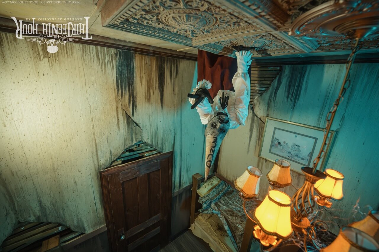 Upside-down scare actor hangs from the ceiling of a decaying bedroom set