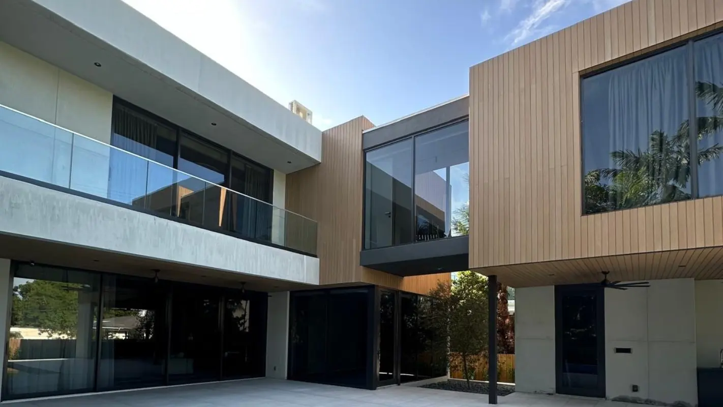 Interior courtyard of Meridian Avenue Residence in South Beach — two-story concrete and wood-clad volumes with glass-railed balcony, floor-to-ceiling sliding doors, and connecting glass bridge by Atelier International.