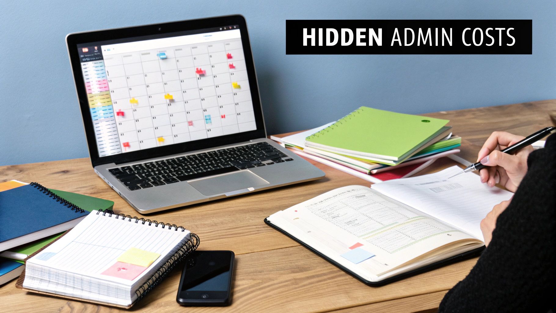 A person writing in a planner on a busy desk with a laptop displaying a calendar, illustrating hidden admin costs.