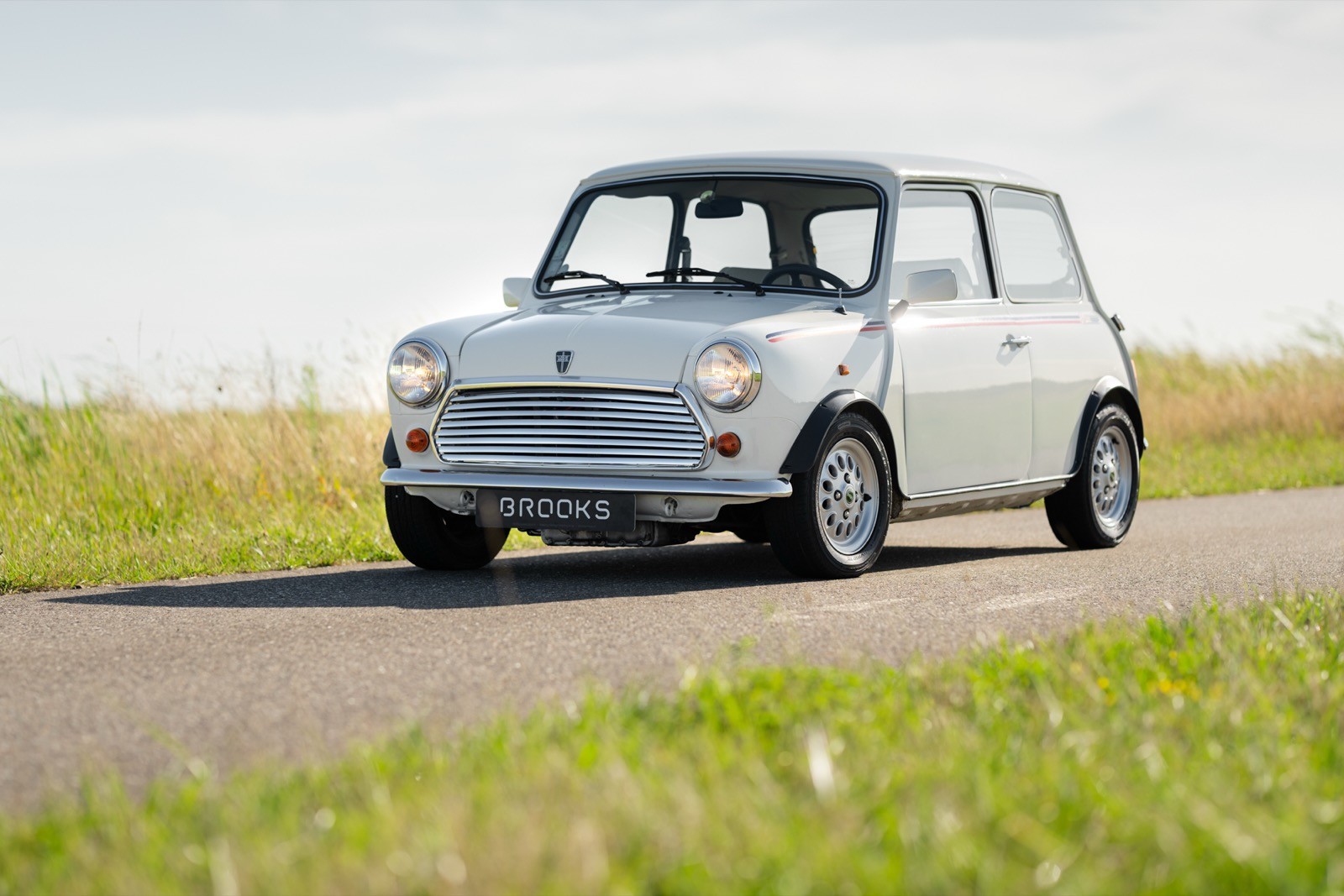 A classic silver car parked on a country road with green grass and a clear blue sky in the background.