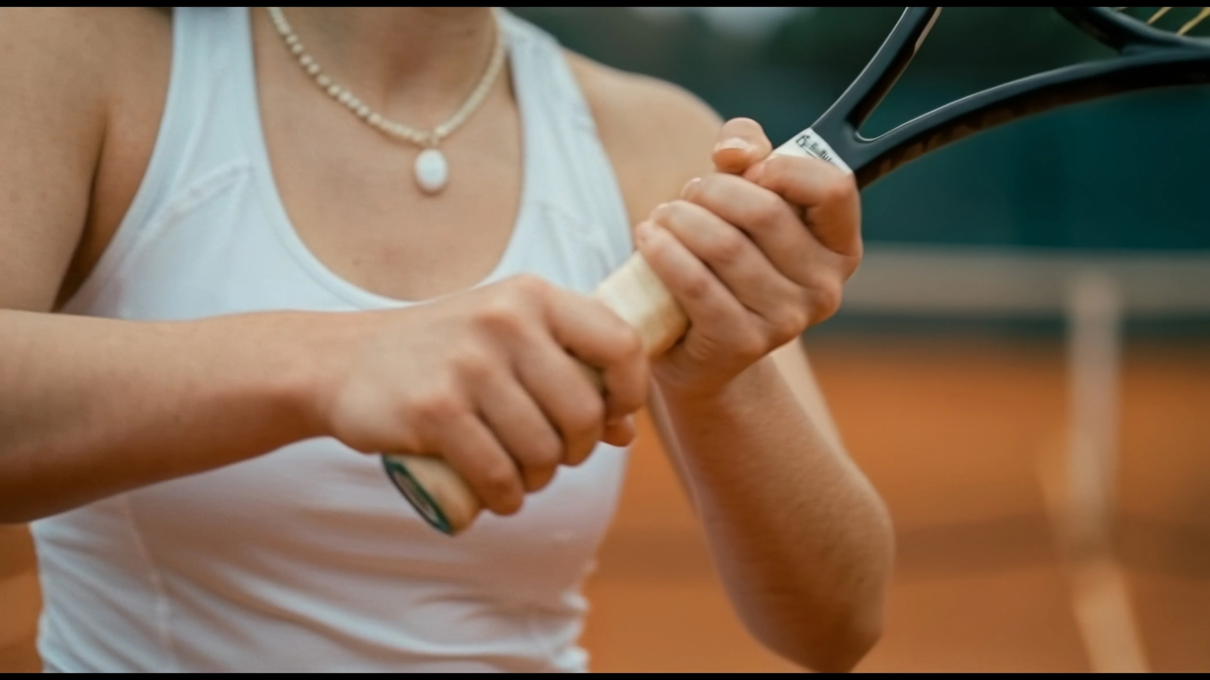 A close-up of a hand holding a brown leather drawstring bag with a gathered top and rounded base featuring small metal feet, against light beige pants that contrast with the rich brown leather.
