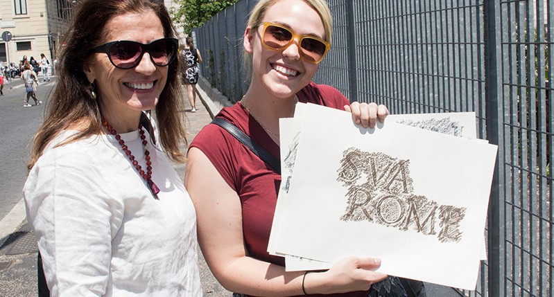 two women holding paper in front of fence