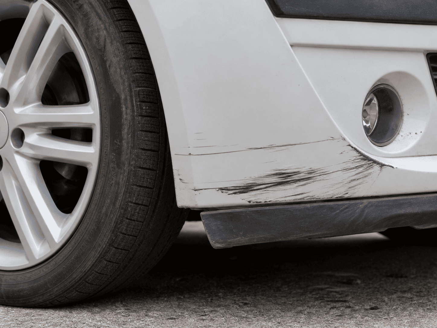 Scratched front bumper and wheel of a white car.