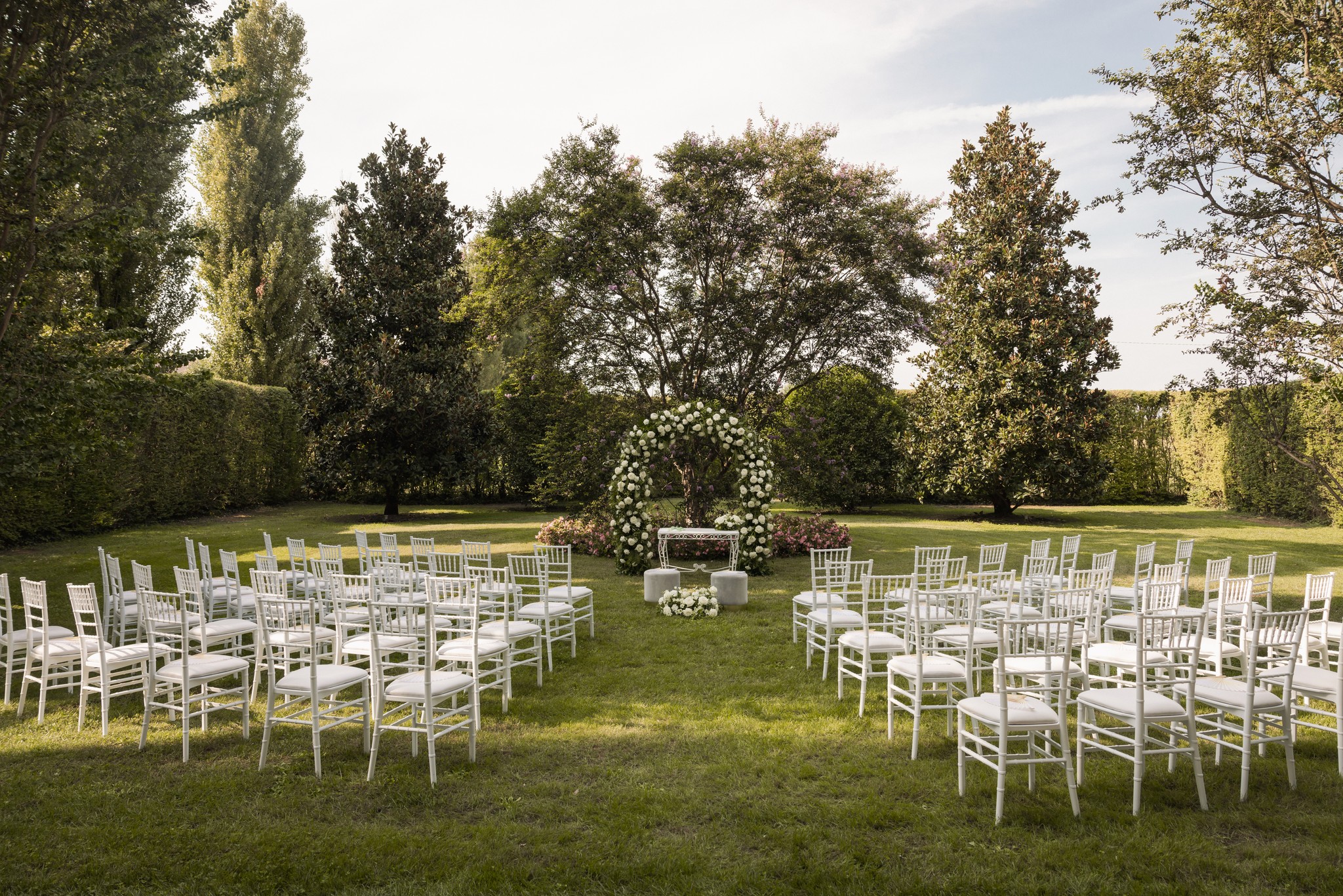 Cerimonia matrimoniale nel giardino di Villa Negri, sedie bianche disposte verso l'altare floreale tra alberi e prato verde