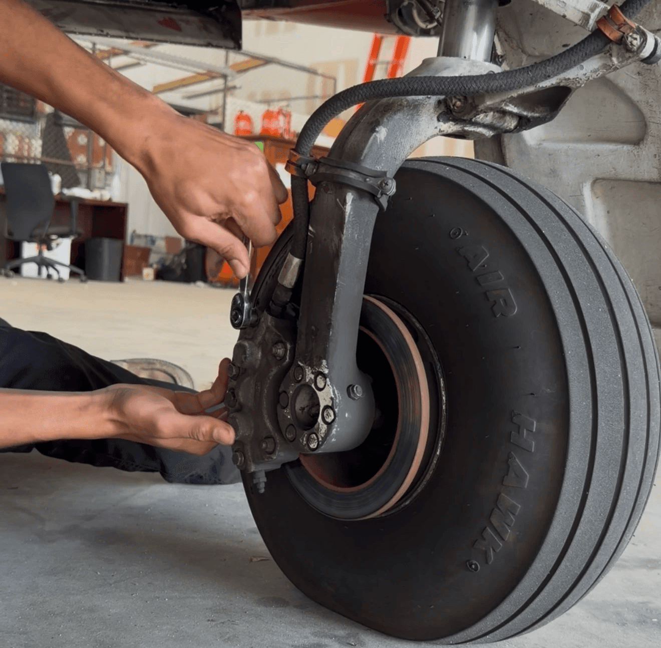 close-up view of a technician's hands using a wrench to perform maintenance on an aircraft's brake assembly and landing gear tire