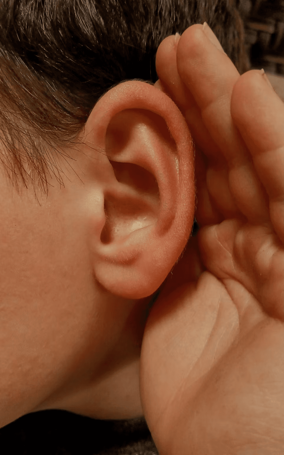 A close up photograph of a hand cupping an ear