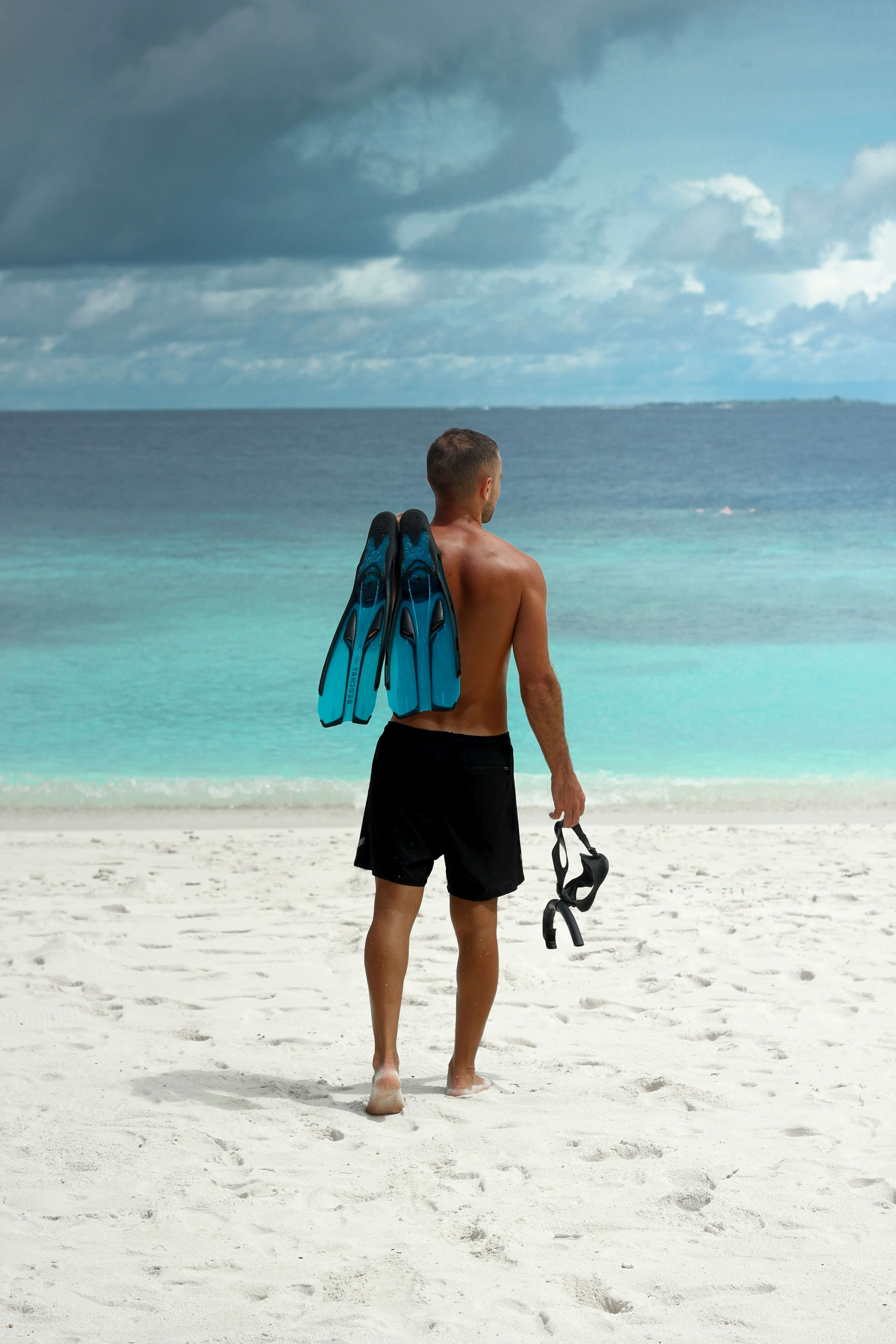 Man standing on a white sandy beach with snorkeling gear, gazing at the turquoise waters near Club Vieques, Puerto Rico.