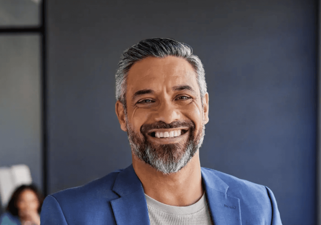 Man with short dark hair and a beard wearing a light shirt, smiling at the camera.