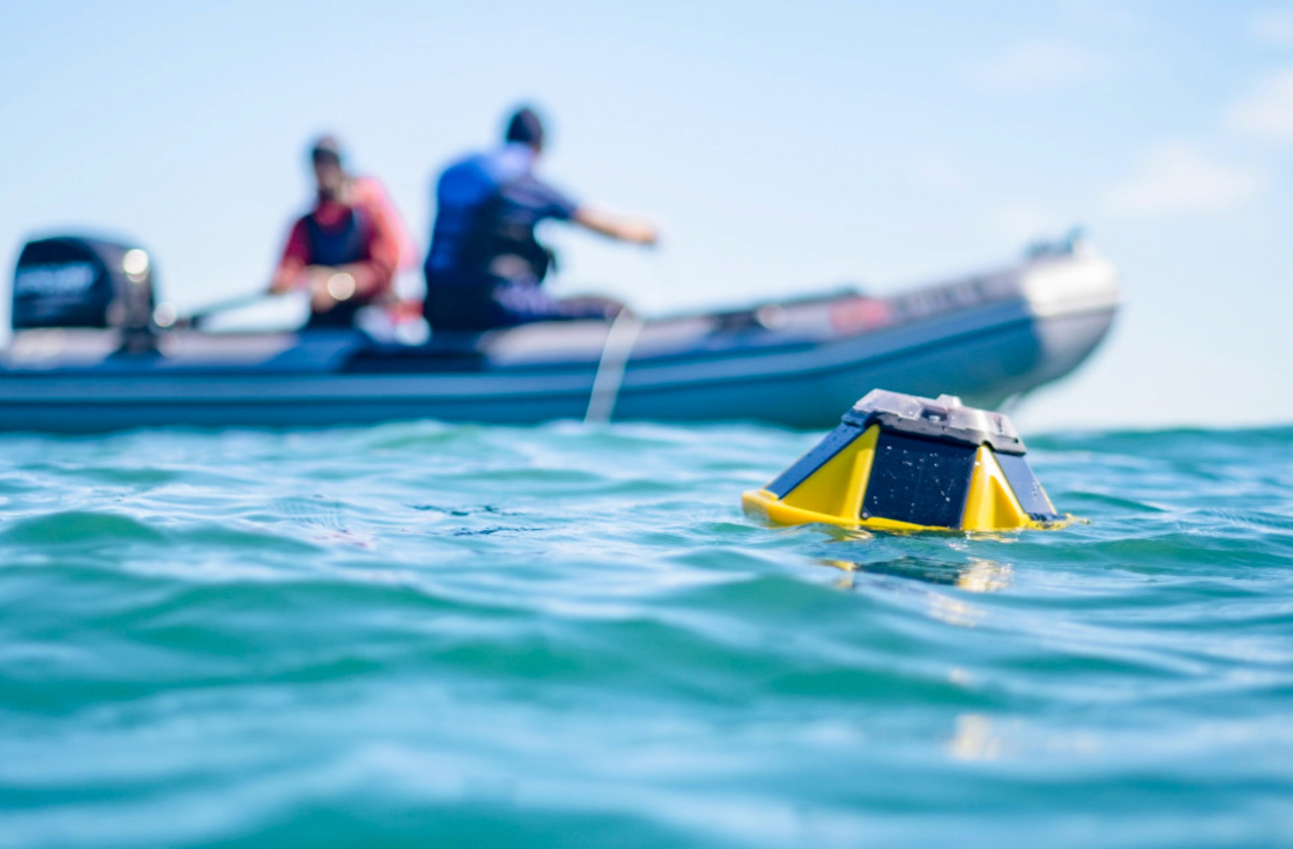 Sofar ocan spotting buoy floating in ocean water, boat with people in background.