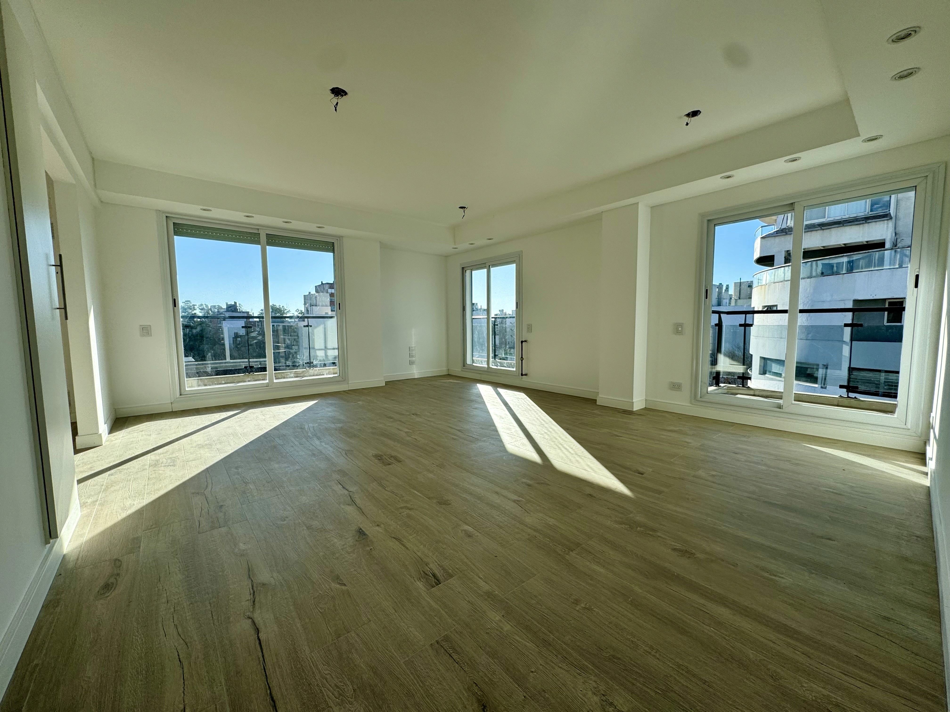 Living amplio con piso de madera, paredes blancas y tres ventanales con balcón y vista a la ciudad, Italia 2003, Rosario