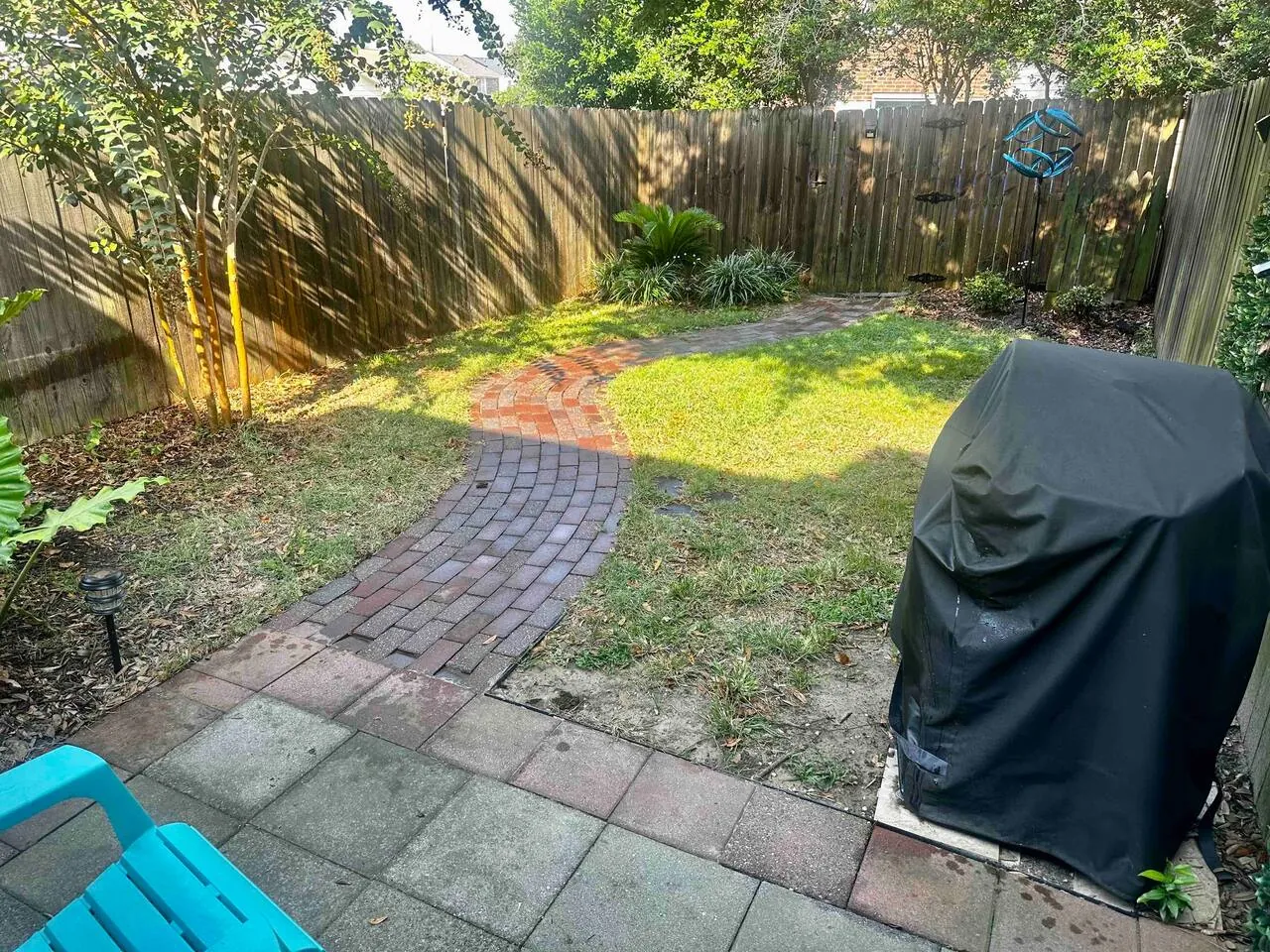Private fenced backyard with a brick path, lawn and covered gas grill