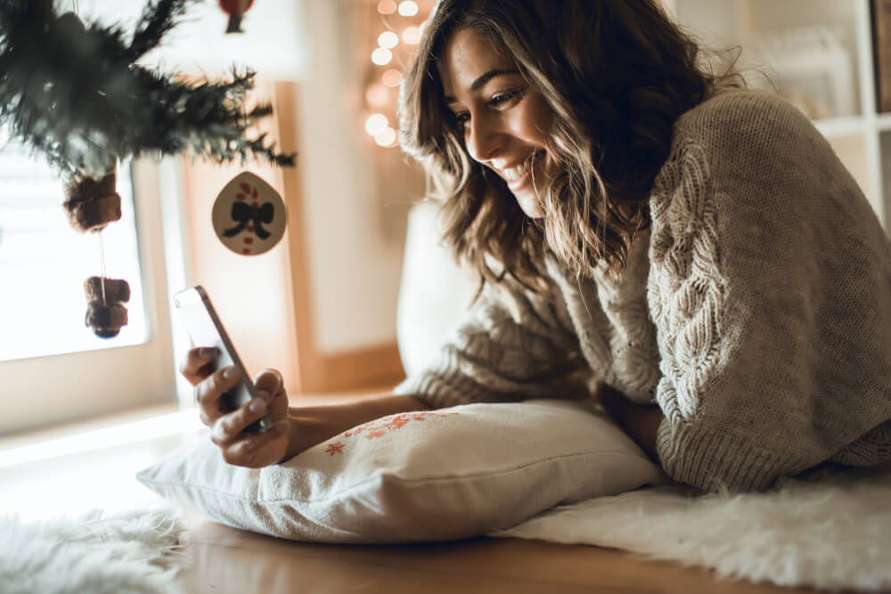Smiling woman using smartphone while lying by Christmas tree