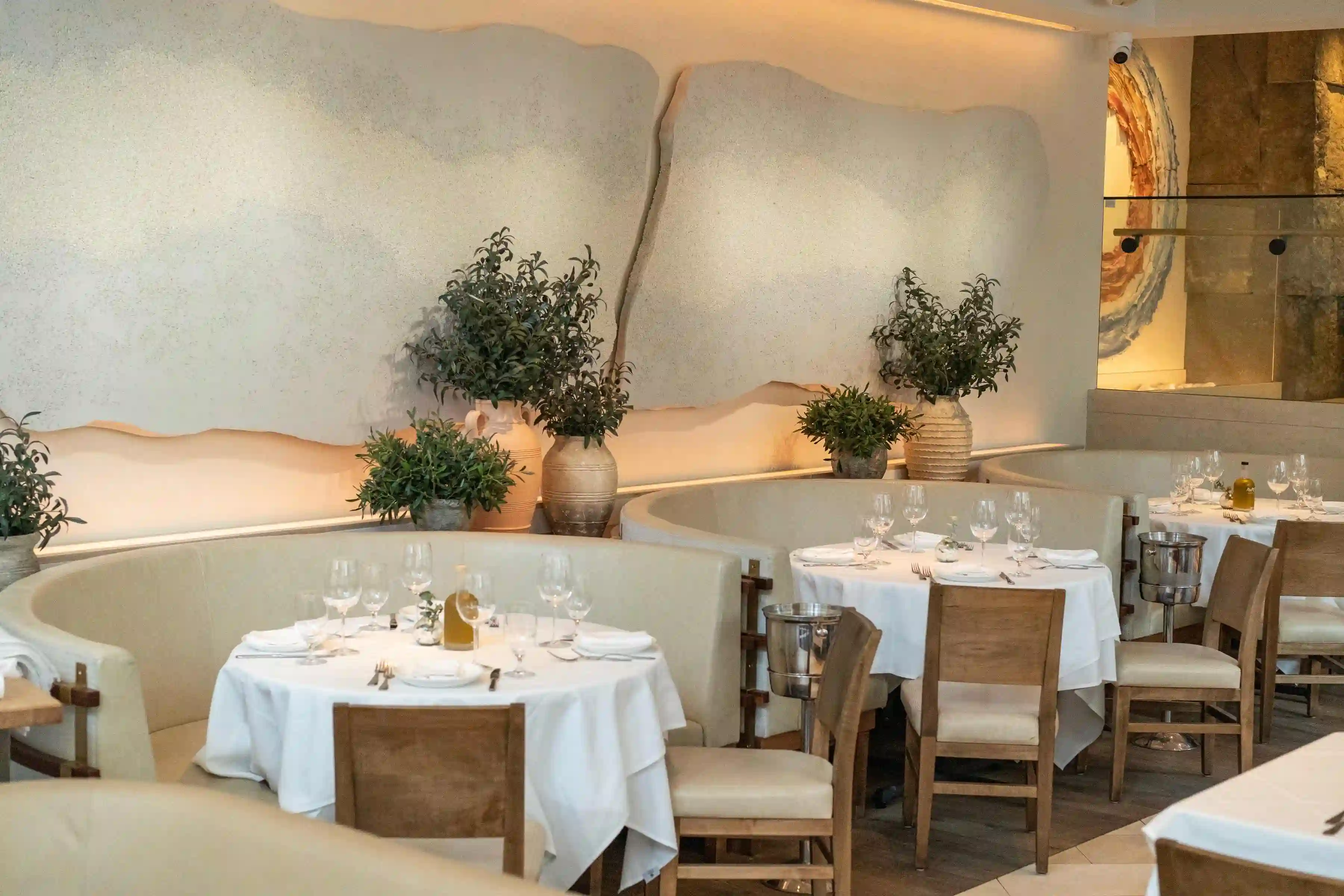 Interior of a modern restaurant, featuring elegant white tables, minimalist decor, and greenery in the background.