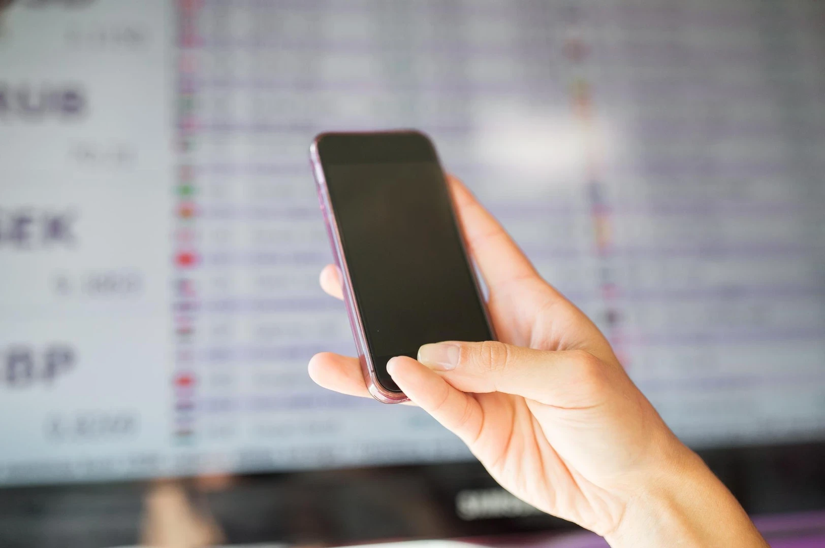 finance, technology, people, currency conversion and money concept - hand with smartphone over exchange rates on digital disp