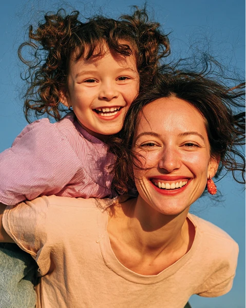 Colorful bird-shaped playground slide with stairs, in a sunny park. Surrounded by trees and shops, it exudes a playful and inviting atmosphere.