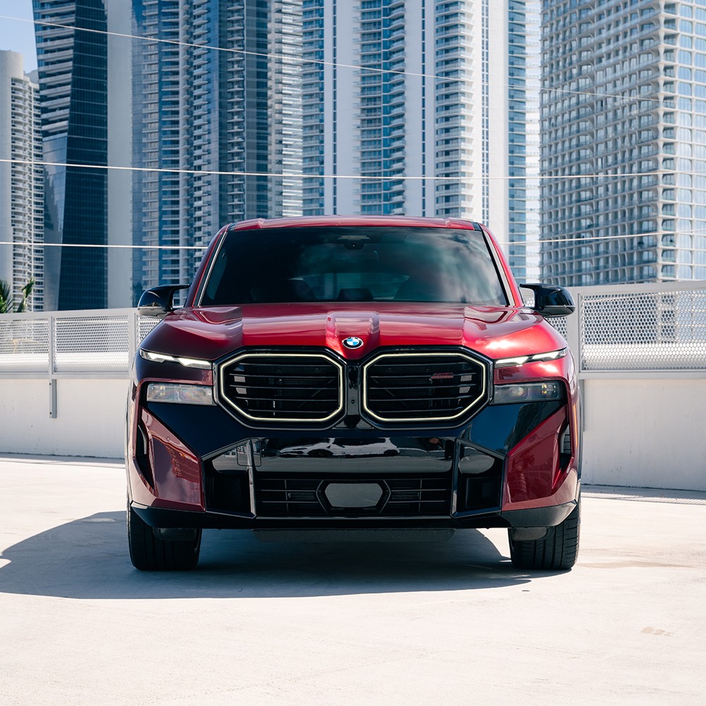 Head-on front view of a red BMW XM Label Red, emphasizing its illuminated grille surround and split headlight design.
