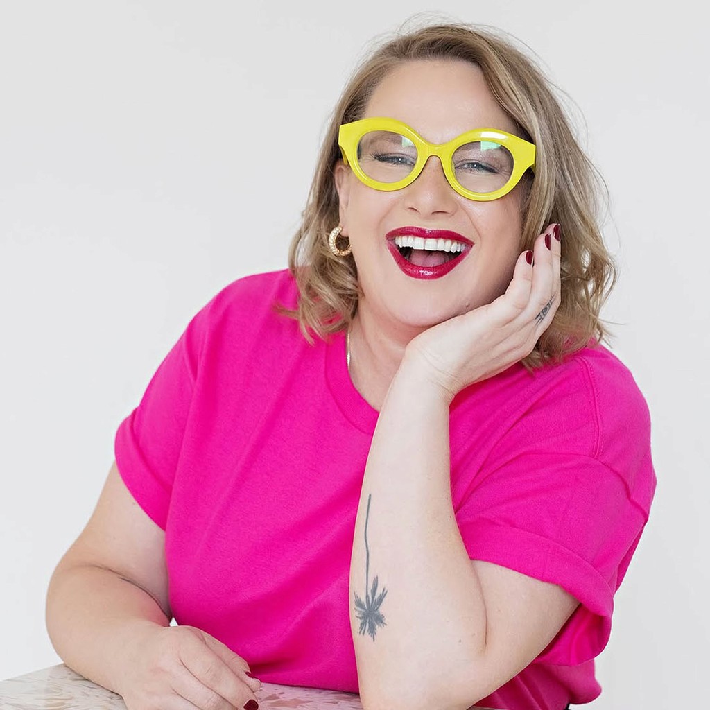 Bright and cheerful portrait captured at Node Studio, featuring a woman in a vibrant pink top and bold yellow glasses, exuding personality against a clean white backdrop