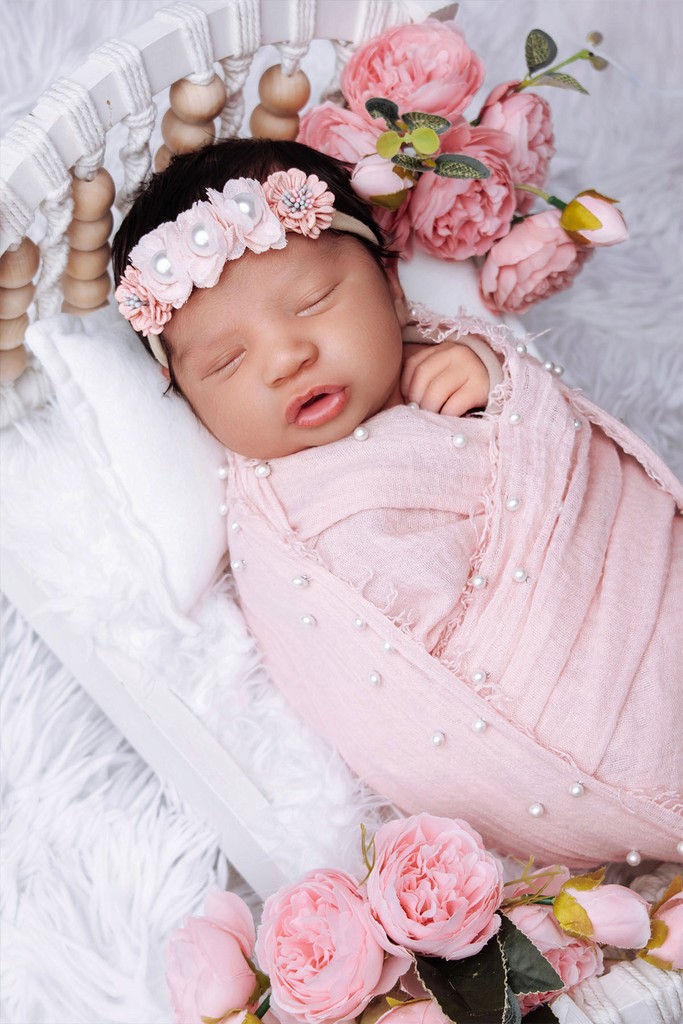 Newborn girl in pink outfit sleeping with soft floral setup at Bloom N’ Baby Studio