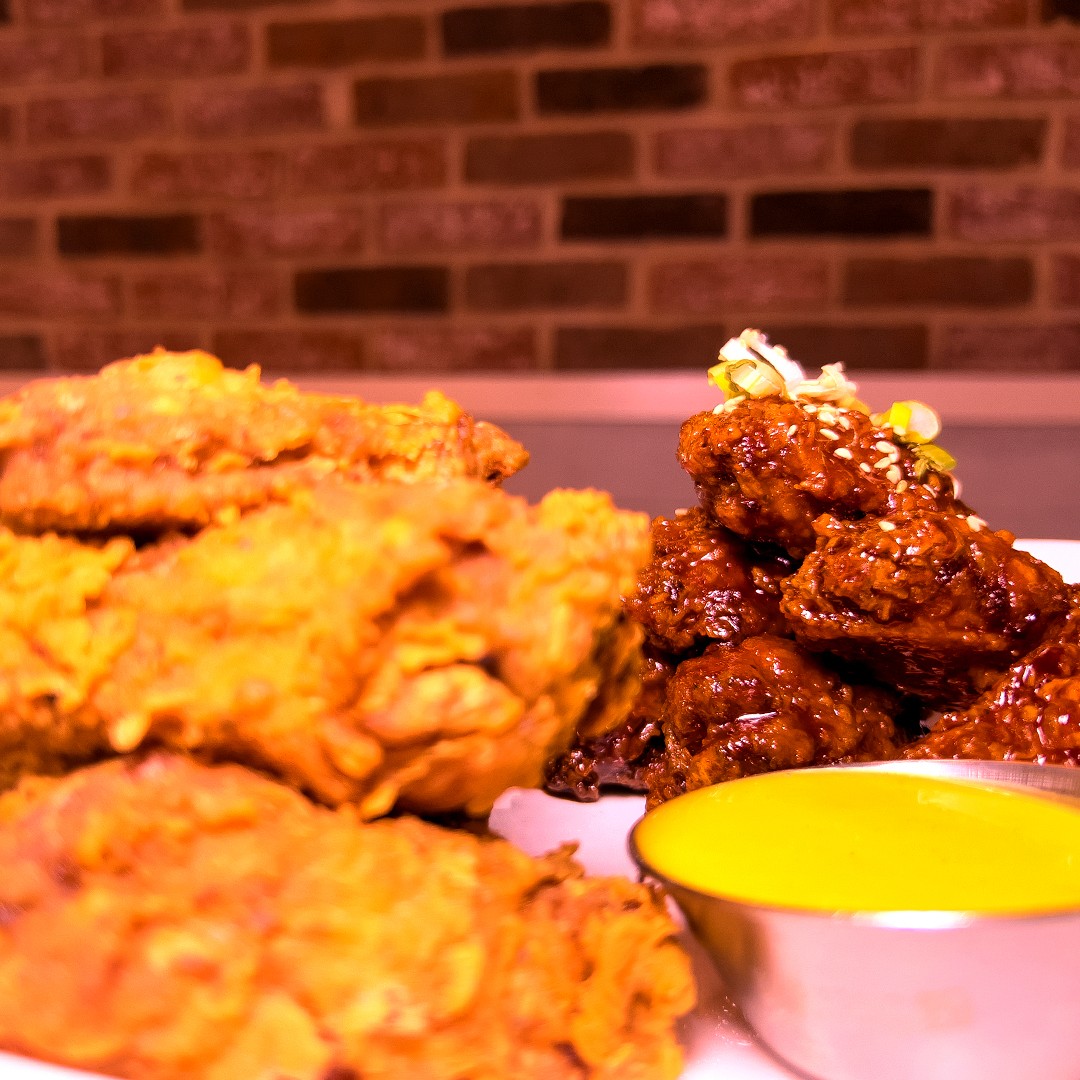 Close-up of Koreanz signature fried chicken and Yangnyeom chicken (sweet and spicy glazed chicken), garnished with sesame seeds and green onions, served with dipping sauce and pickled radish. A perfect representation of authentic Korean BBQ comfort food.