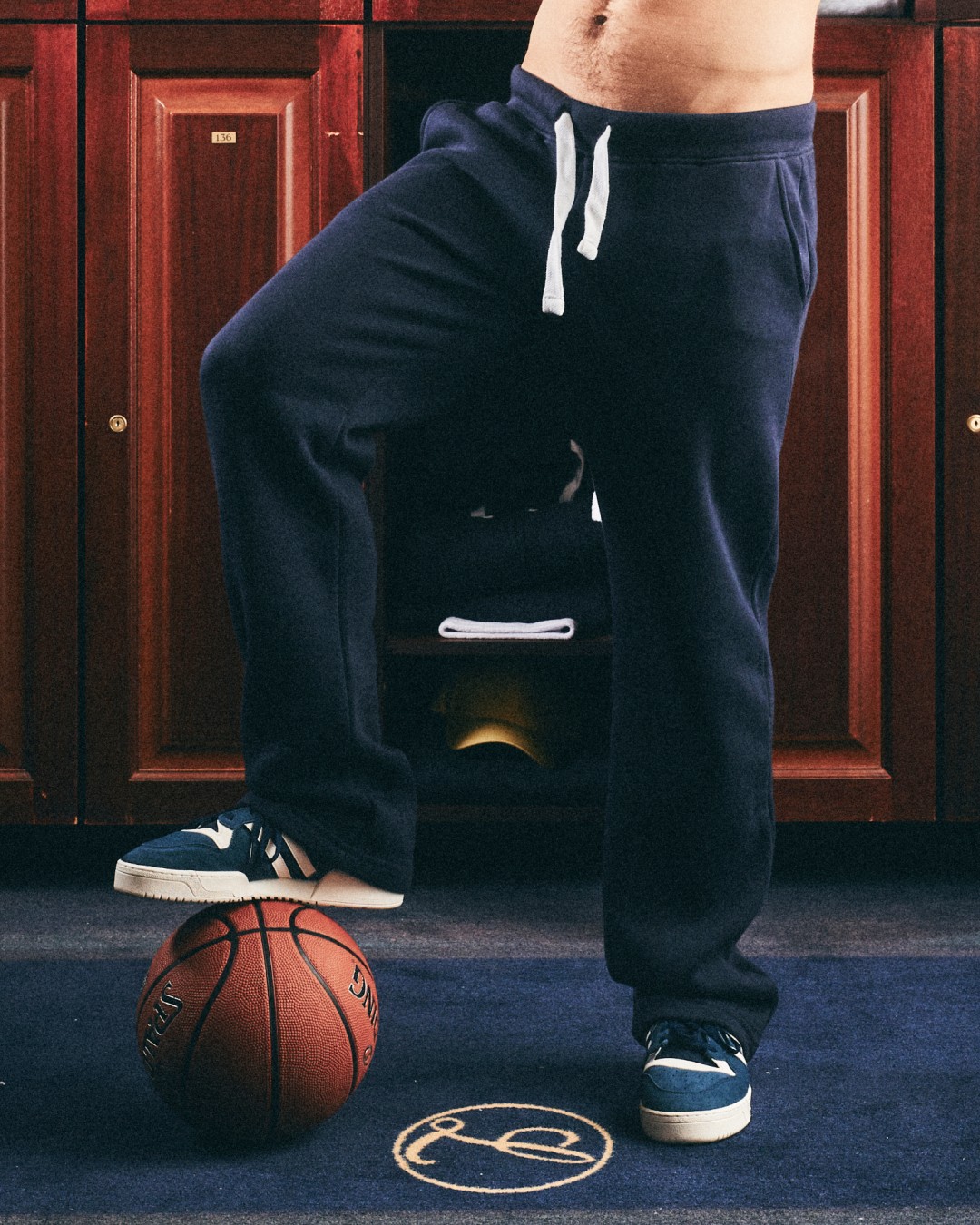 Person wearing a dark navy sweatpant inside a classic locker room with wooden cabinets