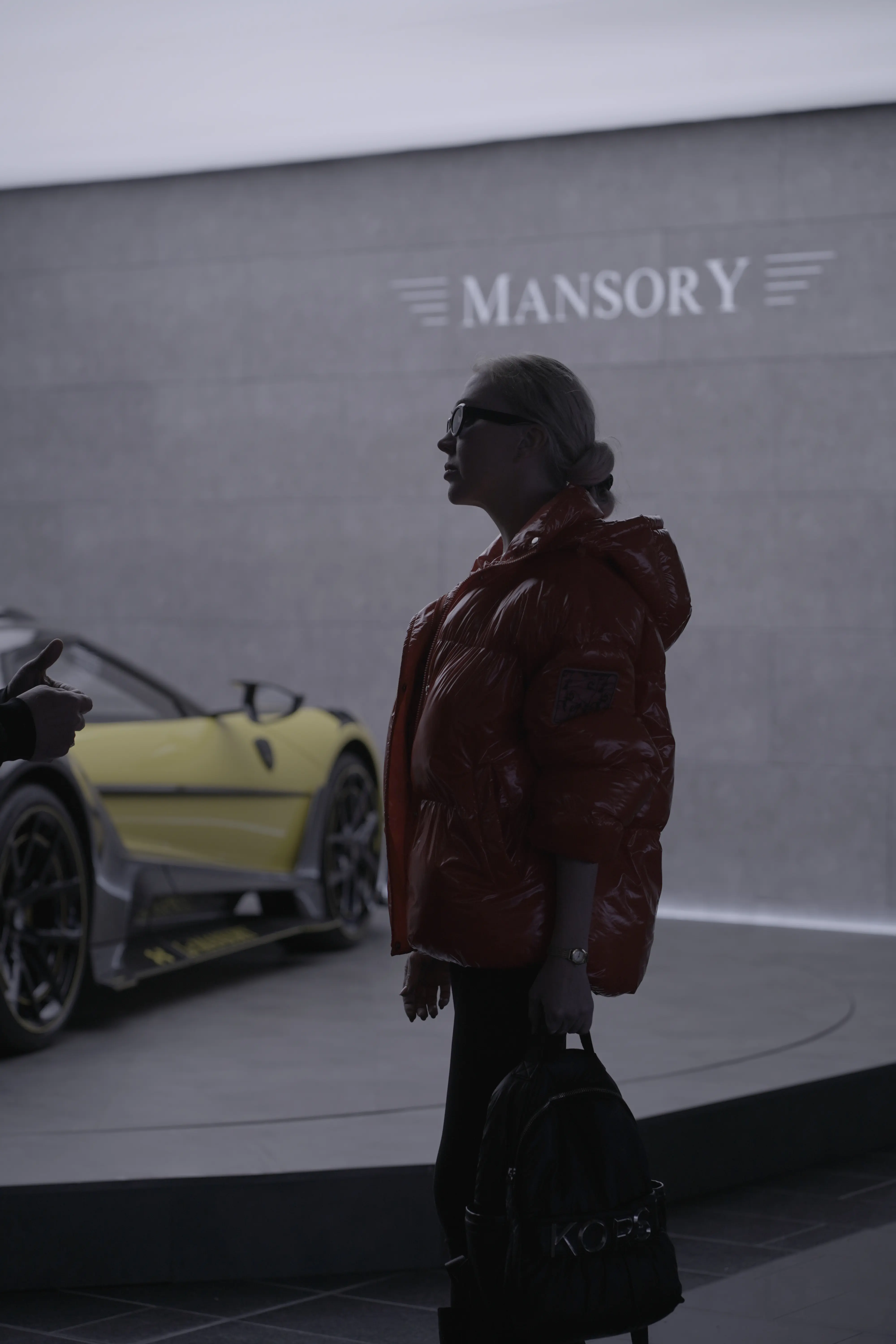Elena standing in front of a yellow Mansory supercar inside the factory during a photoshoot