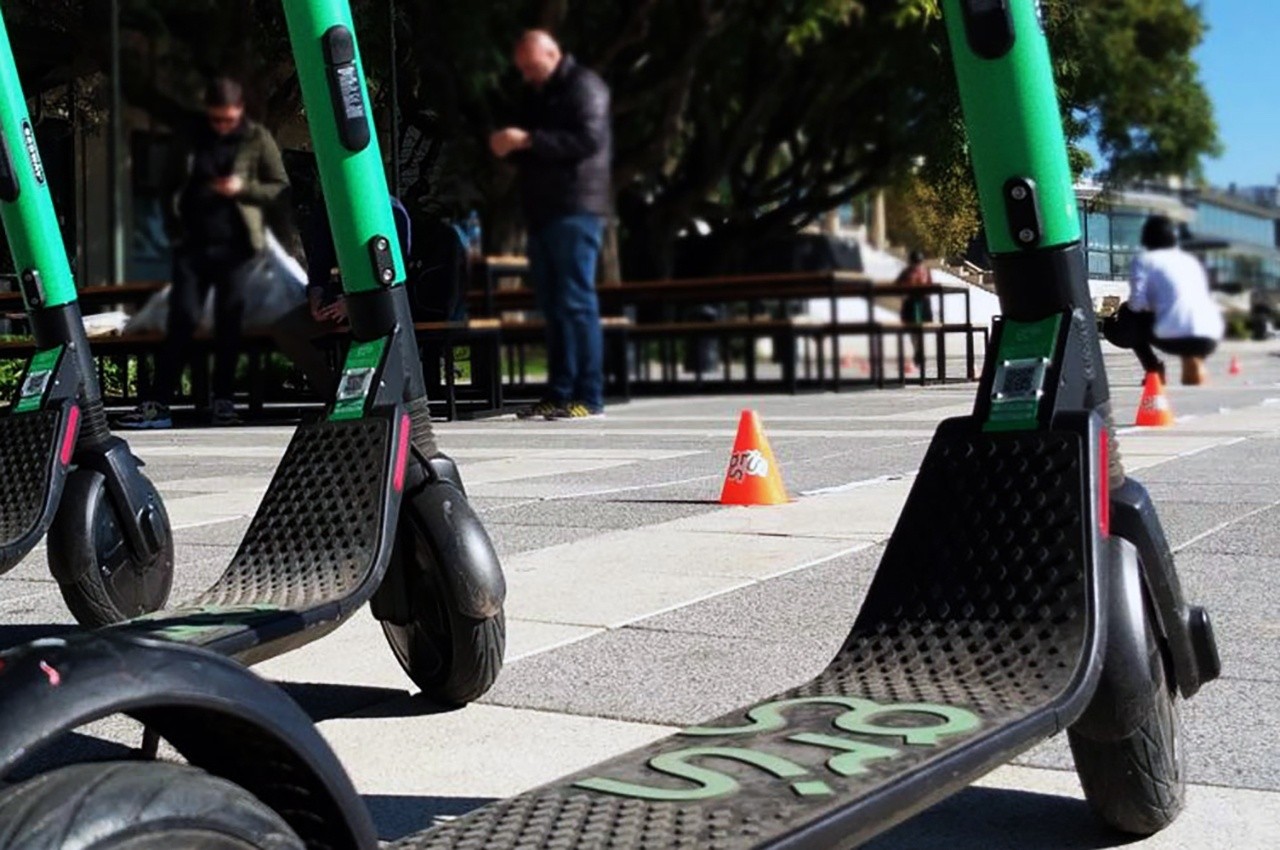 Scooters eléctricos estacionados junto a conos en un espacio urbano.