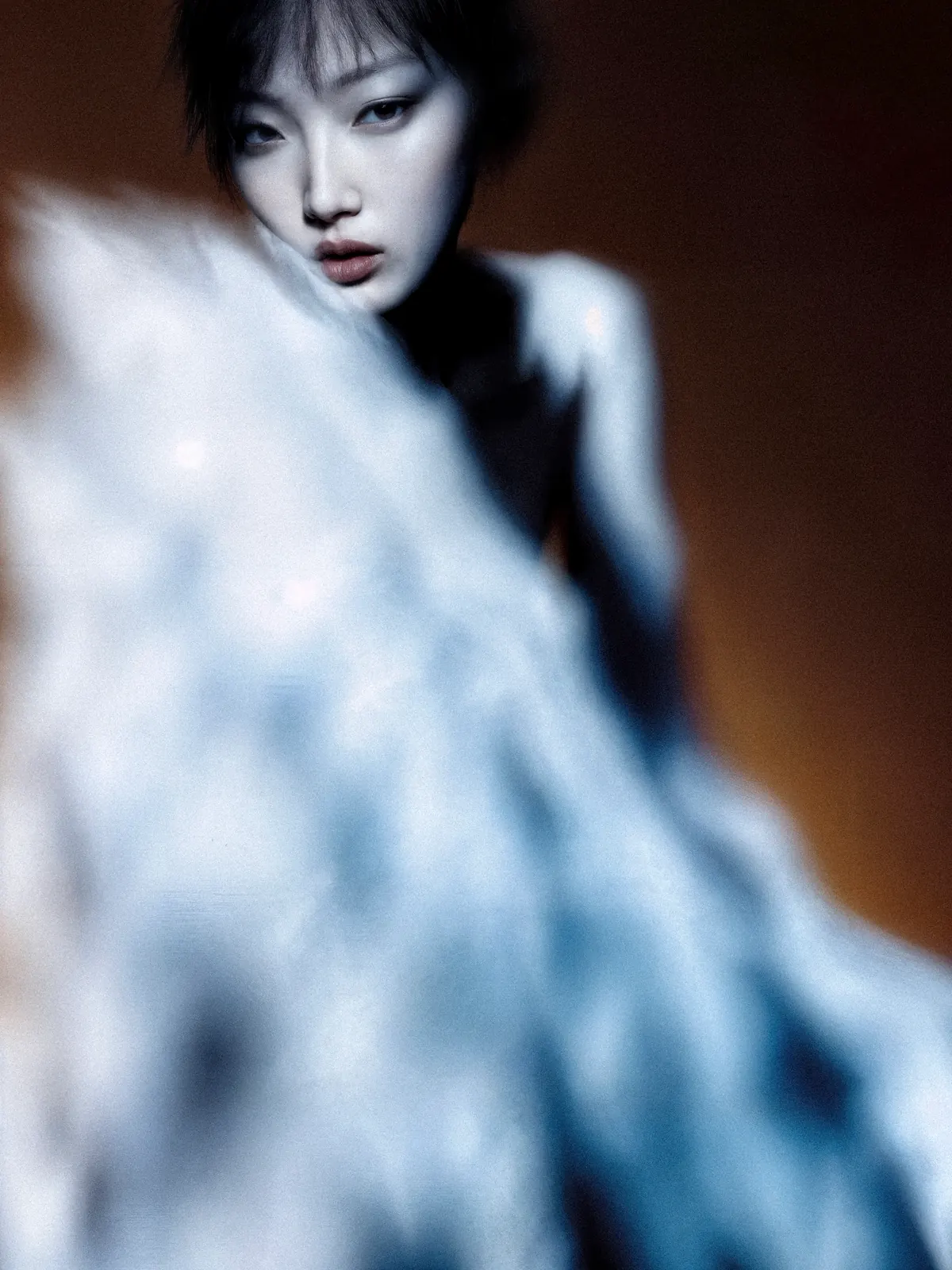 Soft-focus portrait behind flowing pale-blue fabric.